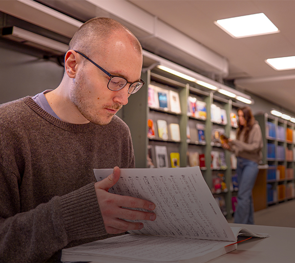 Ung man bläddrar i noter på Musik- och teaterbiblioteket. En ung kvinna rör sig i bakgrunden.