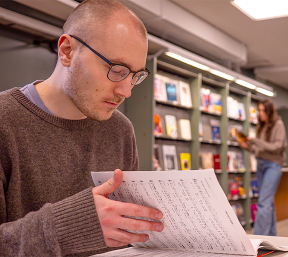 Ung man bläddrar i noter på Musik- och teaterbiblioteket. En ung kvinna rör sig i bakgrunden.