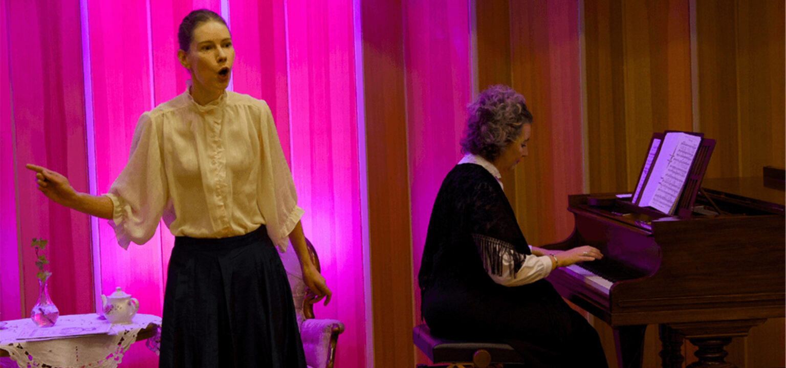 En person i historiska kl&auml;der sjunger, en annan person spelar piano